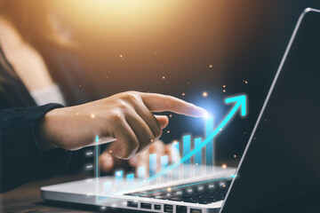Fototapeta premium A businesswoman touching a holographic rising bar chart on laptop, representing business growth, data analytics, performance improvement, and financial success technology concept.
