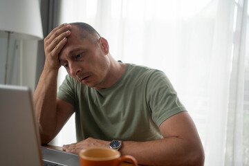 Feeling tired. Frustrated mature man looking exhausted and holding head with hand while sitting at laptop his home working place