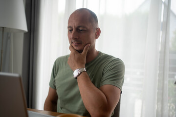 Thoughtful man working from home using laptop thinking about freelance project