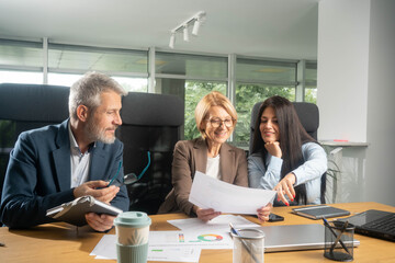 Three busy happy middle aged professional business man and two women executive leaders team using laptop working on computer at work desk having conversation on financial project at meeting in office.