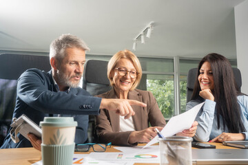 Three busy happy middle aged professional business man and two women executive leaders team using laptop working on computer at work desk having conversation on financial project at meeting in office.