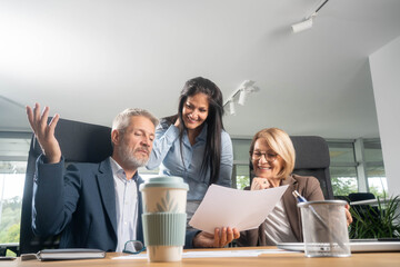 Three busy happy middle aged professional business man and two women executive leaders team using laptop working on computer at work desk having conversation on financial project at meeting in office.