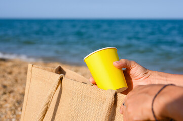 Paper disposable cup in hand on the beach. Close-up, selective focus