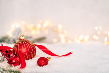 Red and gold Christmas baubles with ribbon resting on snow, surrounded by warm fairy lights in a cozy, festive holiday setting. Ideal for holiday greeting cards, festive banners.