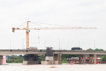 tower crane over river bridge under construction with traffic on roadway