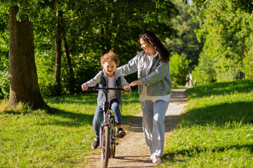 Happy smiling mother teaching boy how to balance or ride bicycle. Child development concept. Outdoor activity with kids.