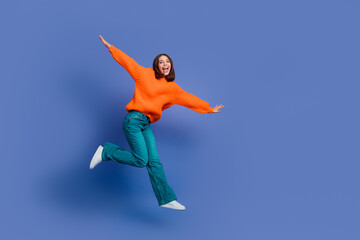 Obraz premium Jumping woman in orange sweater and blue jeans with happy expression against solid background celebrating movement and joy