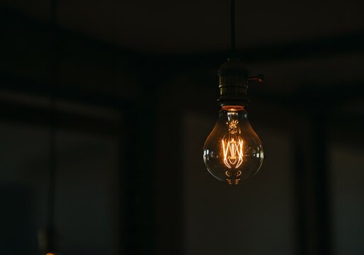 Vintage illuminated light bulb hanging from the ceiling, radiating a warm glow in the dimly lit room