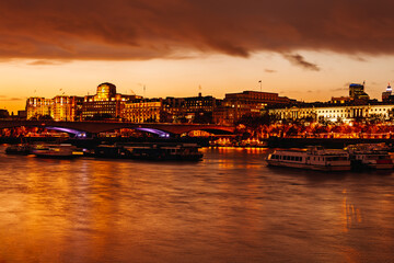 Illuminated buildings along the River Thames at sunset with reflections and boats in London