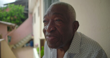 One Elderly Black man sitting on a chair on a porch, looking into the distance with a serene expression, tropical setting, pink building, stairs in the background
