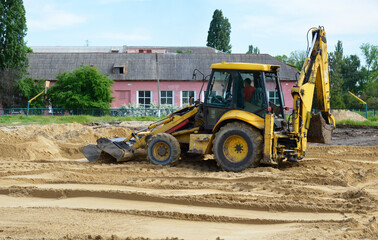 a yellow tractor with a blade and a bucket levels the sand at a construction site. construction machinery doing hard work