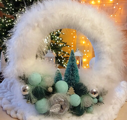 A fluffy Christmas wreath with spruce branches and pine cones against the blurred glow of a bright garland. Decorating your home for Christmas and New Year's celebrations. A cheerful mood.