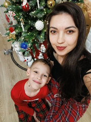 A woman and a boy sitting on the floor in front of a decorated Christmas tree. Garlands, ornaments, and baubles glitter on the tree. The comfort and joy of a family holiday