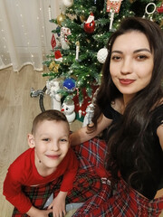 A woman and a boy sitting on the floor in front of a decorated Christmas tree. Garlands, ornaments, and baubles glitter on the tree. The comfort and joy of a family holiday