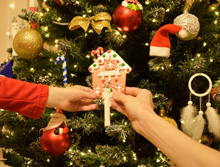 Women's and children's hands hang a Christmas tree decoration. Celebrating New Year and Christmas. Warmth, comfort, and a cheerful atmosphere.