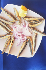 small fish deep-fried with lemon and herbs on a white plate. light and tasty snack for beer. seafood at the beach cafe