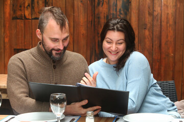 Cheerful middle-aged couple sitting in a rustic restaurant, looking at the menu and enjoying time together.