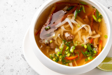 Traditional Vietnamese pho soup with beef slices, rice noodles, chili, herbs, and lime wedge in a white bowl. Authentic Asian cuisine, top view, isolated on white background