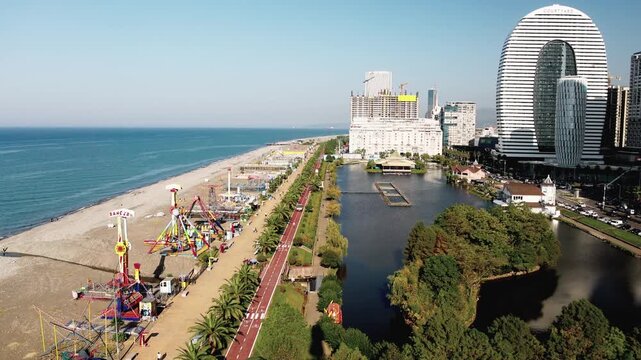 Batumi Embankment. A beach with a pier and a large building in the background. The pier has a lot of rides and the building is very tall