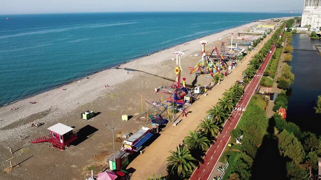 Batumi Embankment. A beach with a pier and a large building in the background. The pier has a lot of rides and the building is very tall