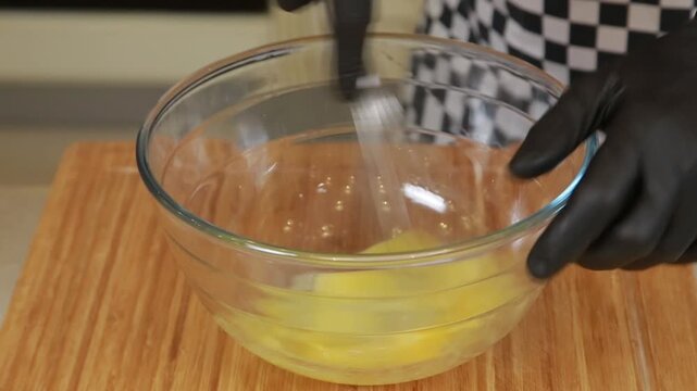 Chef is beating eggs in a glass bowl while cooking omelet