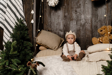 A boy like a little prince with a crown on his head sits on mattresses with pillows