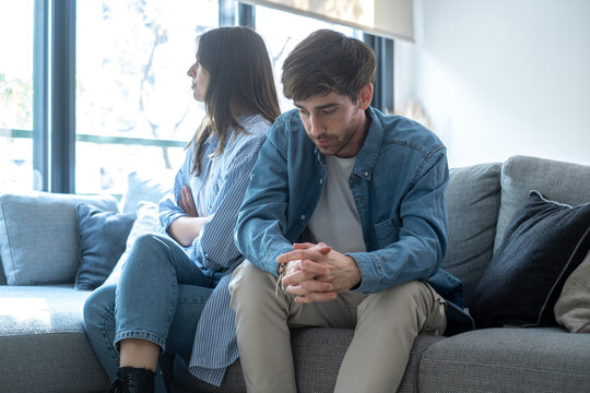 Young couple sitting on sofa at home arguing and confronting each other, concept of relationship problems, breakup, jealousy, betrayal, lack of trust, or communication issues