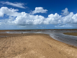 Obraz premium Sandy expanse meeting a clear sky filled with puffy clouds over shallow coastal waters in Porto Seguro