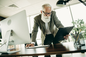 Senior businessman working in a modern office, focusing on charts, displaying confidence and professionalism