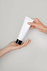 Female hand passing a tube of cream to another hand. Woman's hand hold cream tube. Cosmetic product branding mockup. Daily skincare and face care routine. Cosmetic product mock up, template, close up