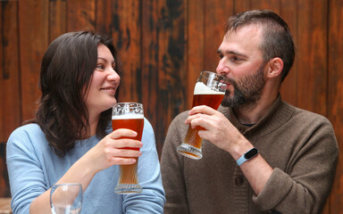 Cheerful middle-aged couple in a rustic restaurant enjoying drinks together, smiling and talking over tall beer glasses.