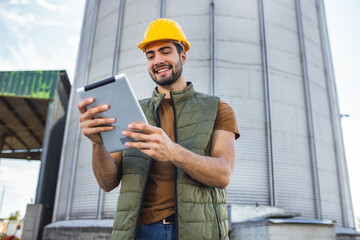 Young worker standing in front of silo holding tablet