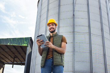 Young worker standing in front of silo holding tablet