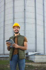 Young worker standing in front of silo holding tablet