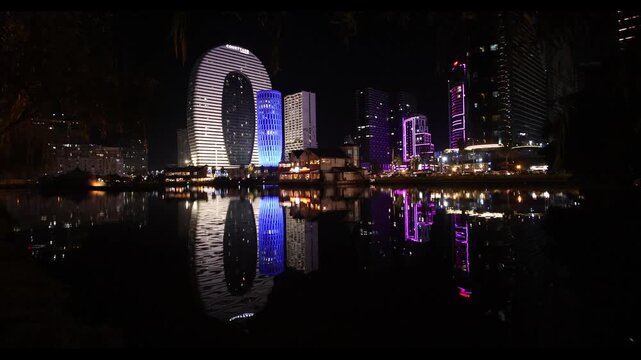 Night panorama of the city of Batumi. Hotels, skyscrapers and apartments located near the singing fountain. Reflections of buildings in the water