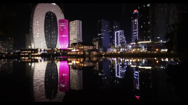 Night panorama of the city of Batumi. Hotels, skyscrapers and apartments located near the singing fountain. Reflections of buildings in the water