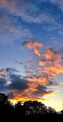Colorful sunset sky with glowing clouds over silhouette trees-Vibrant sunset with intense orange and purple hues above dark tree silhouettes. Dramatic evening sky with glowing clouds.