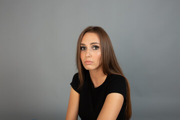 Obraz premium Close-up portrait of a young woman with elegant evening makeup. Smoky eyes, nude lips, and smooth hair. Studio shot on gray background. Beauty, cosmetics, and fashion concept.