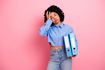 Young woman with curly hair wearing casual attire holding folders against a pink background...
