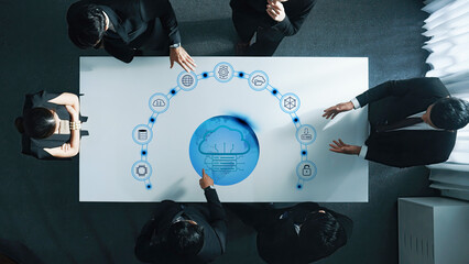 A group of business professionals collaborates around a table showcasing digital cloud technology and data visualization, emphasizing teamwork and innovation in a modern setting. Trope