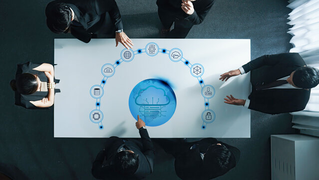 A group of business professionals collaborates around a table showcasing digital cloud technology and data visualization, emphasizing teamwork and innovation in a modern setting. Trope