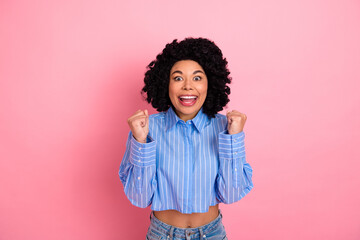 Cheerful young woman celebrates with joyful expression while standing against a vibrant pink...