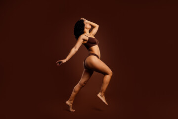 Elegant young woman posing artistically in activewear against a rich brown backdrop showcasing confidence and style