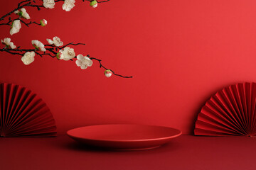 Red empty plate with symmetrical paper fans and cherry blossoms. Happy Chinese New Year 2026 concept.
