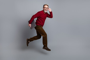 Mature businessman in casual attire confidently posing with a laptop against a minimalist gray background