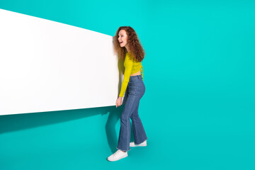 Young woman with curly hair and stylish casual outfit presenting a blank banner against a vibrant...