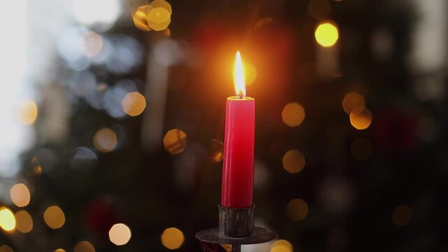 Burning christmas red candle on background of christmas tree twinkling golden lights bokeh. Merry Christmas and Happy Holidays! Christmas advent, holiday candlelight background video