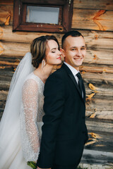 Naklejka premium Bride in an elegant white gown and groom in a classic suit pose by a rustic wooden wall. She holds a bouquet of white flowers. A warm atmosphere of love, style, and intimate romance.