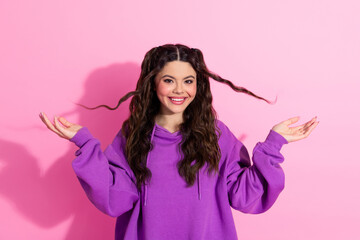 Cheerful young woman posing with wavy hairstyle, wearing a purple sweatshirt against a vibrant pink background