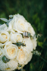 Wedding rings resting on a bouquet of white roses and eucalyptus. Symbol of love, fidelity, and celebration. Elegant floral composition in natural light.
